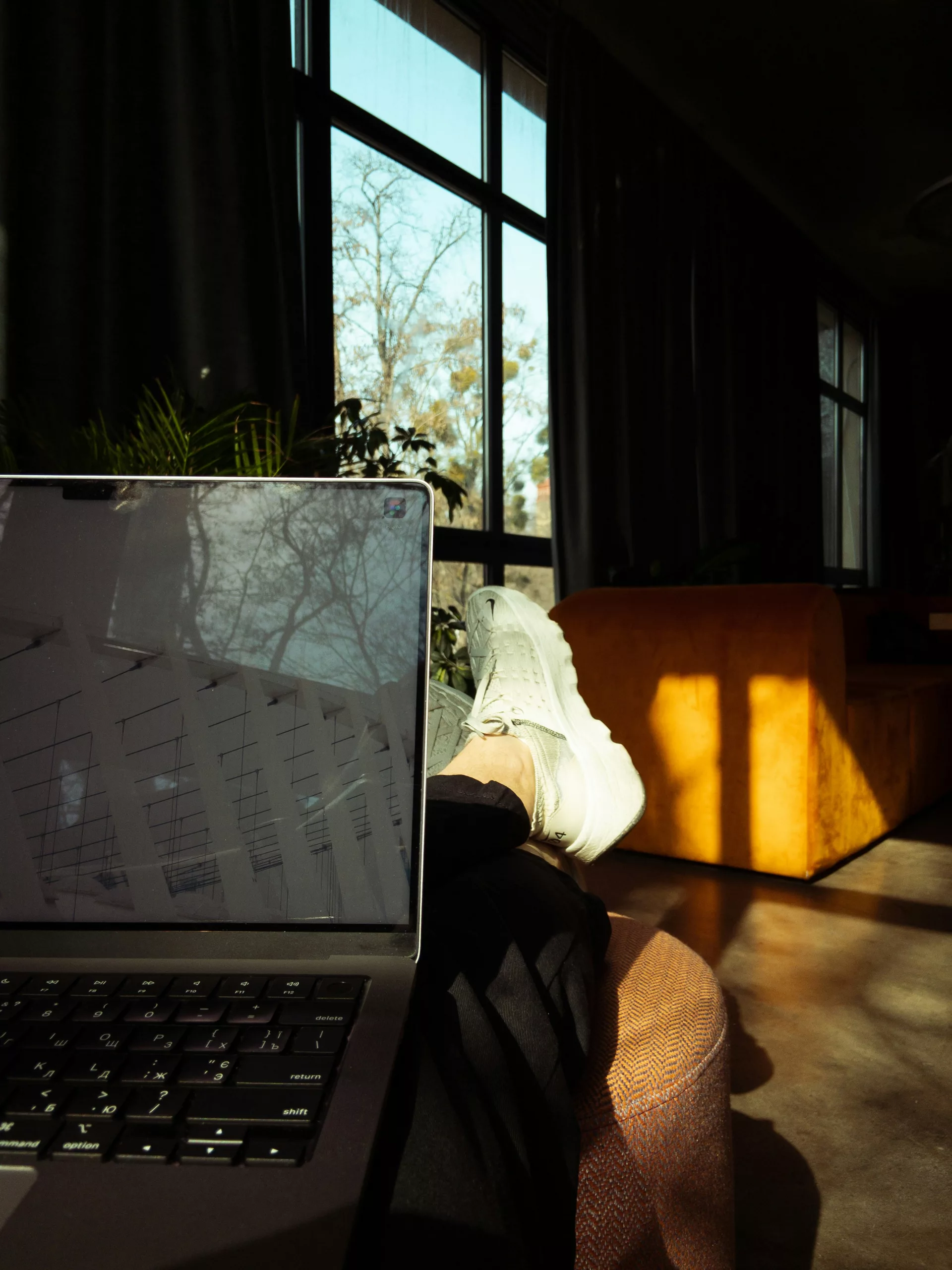 Une personne assise à un bureau moderne et minimaliste, travaillant sur un ordinateur portable, avec une vue sur la ville depuis la fenêtre, illustrant l