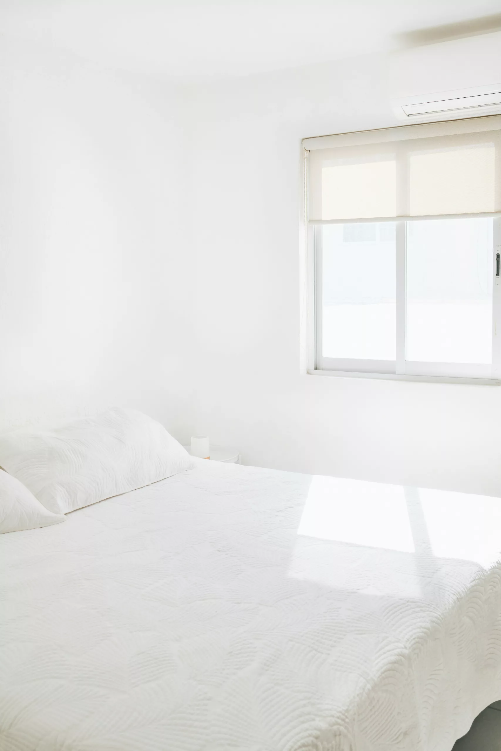 Bright, airy bedroom setup with white linens, specialized lighting, and minimalist decor suitable for Airbnb listing