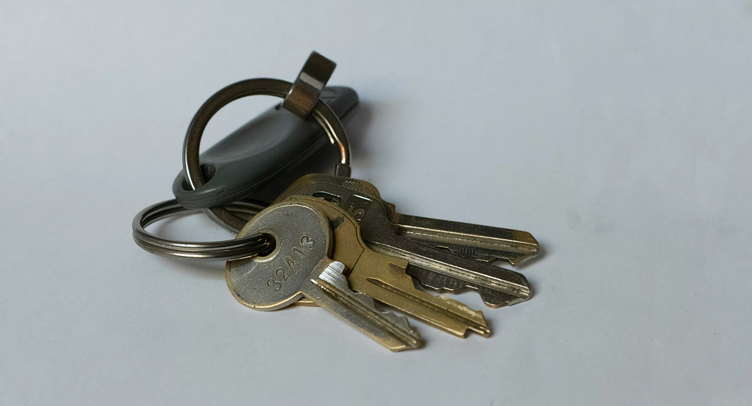 Close up of a hand holding a set of keys with a house keychain, representing property management handover