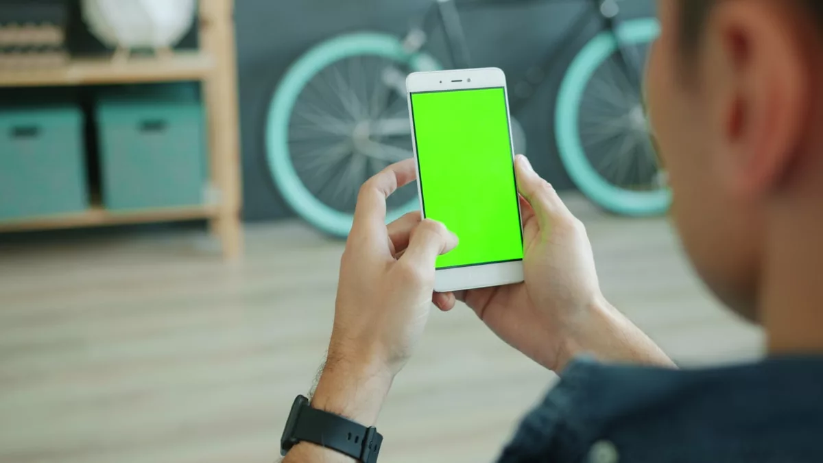 Person holding a smartphone with a green screen.