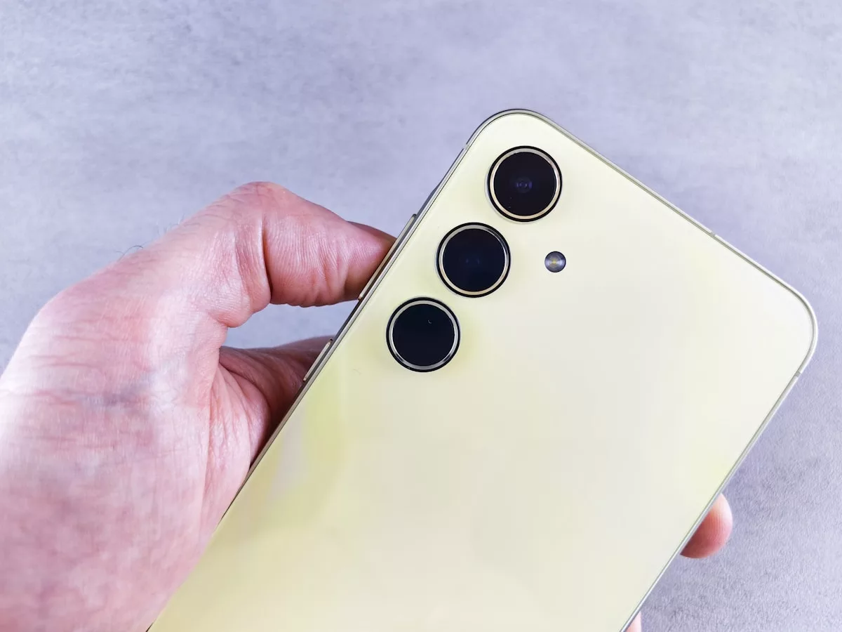 A hand holds a yellow smartphone with cameras.