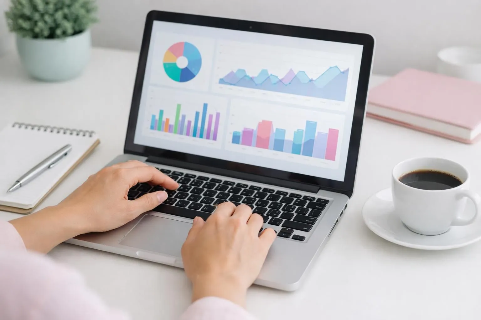 Modern laptop displaying vacation rental analytics dashboard with colorful graphs showing occupancy trends, revenue charts and booking metrics, professional workspace setting with notepad and coffee cup