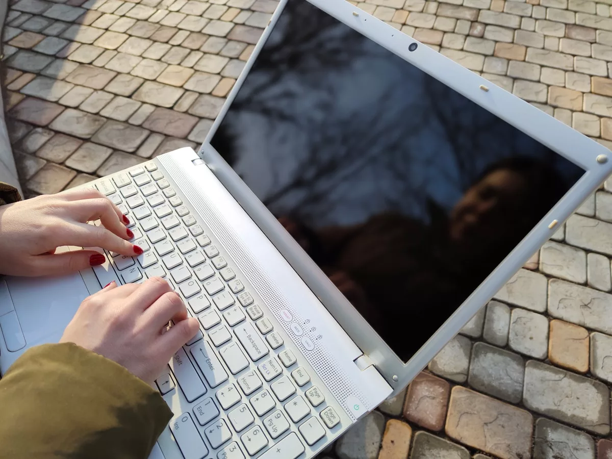 a woman is typing on a laptop outside