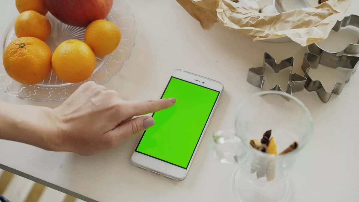 Hand touching a smartphone with a green screen.