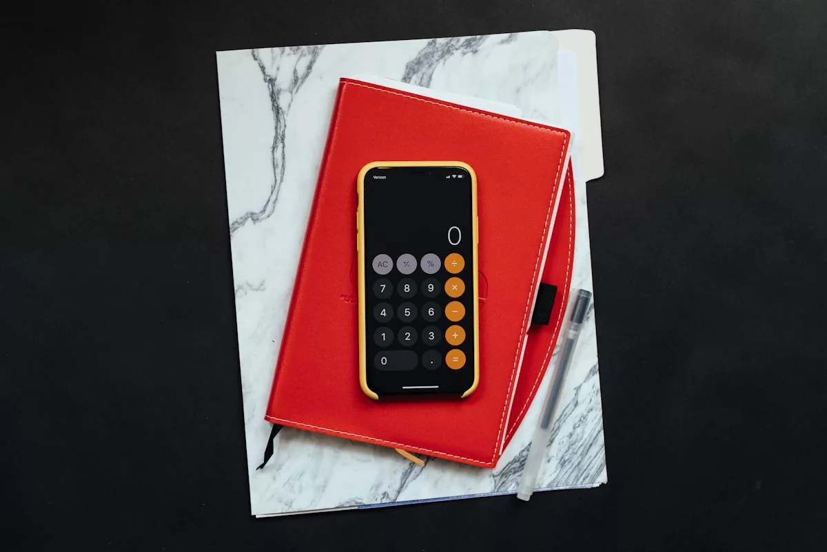 Calculatrice sur un cahier rouge sur un fond de marbre blanc.